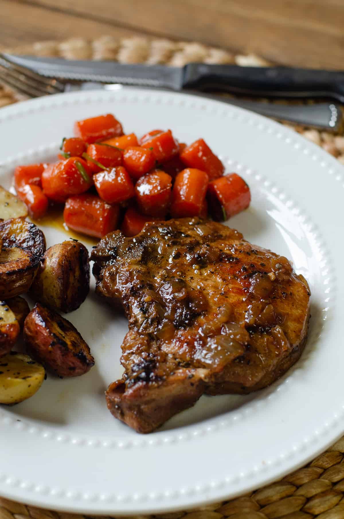 A pork chop on a white plate with carrots and potatoes.