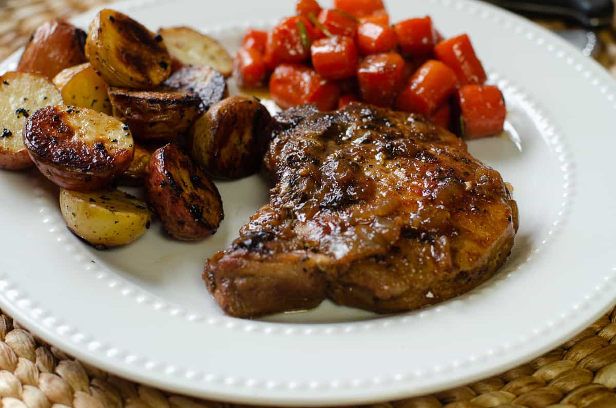 A pork chop on a white plate with carrots and potatoes.