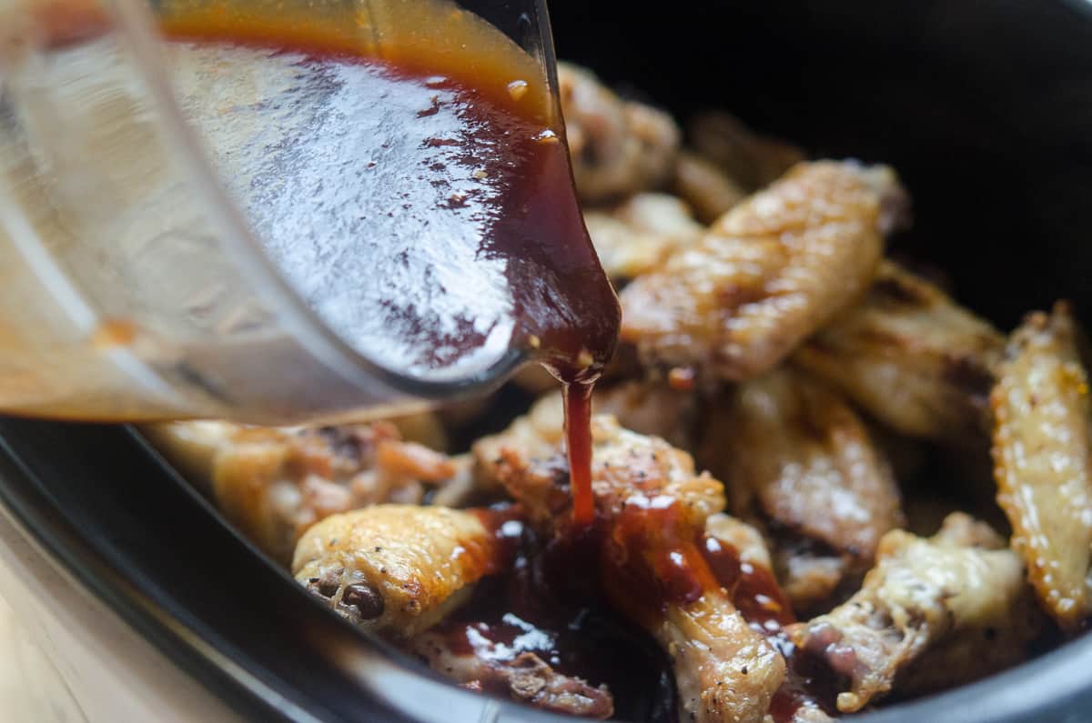 BBQ sauce pouring on to chicken wings in a slow cooker.