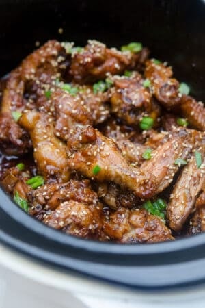 Asian BBQ Wings topped with sesame seeds and green onion in a slow cooker.