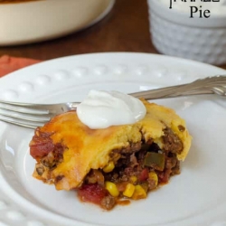 A serving of tamale pie topped with sour cream on a white plate.