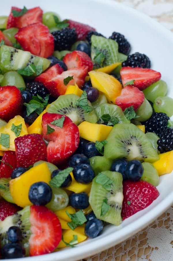 A close up of fruit salad topped with fresh mint.