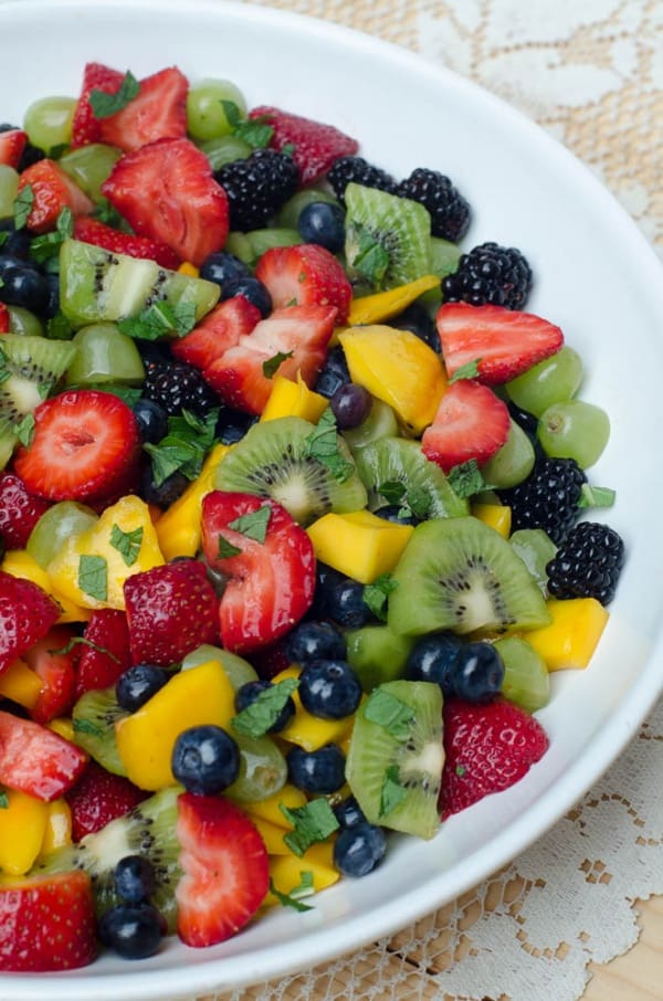 Fruit Salad with Sweet Lime Dressing in a white serving bowl on a lace tablecloth.