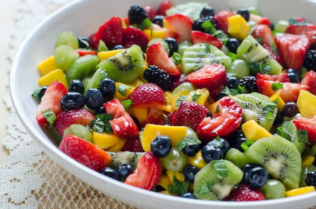 Fruit Salad with Sweet Lime Dressing in a white serving bowl on a lace cloth.