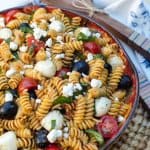 A bowl filled with pasta salad with tomatoes, olives, and cheese.