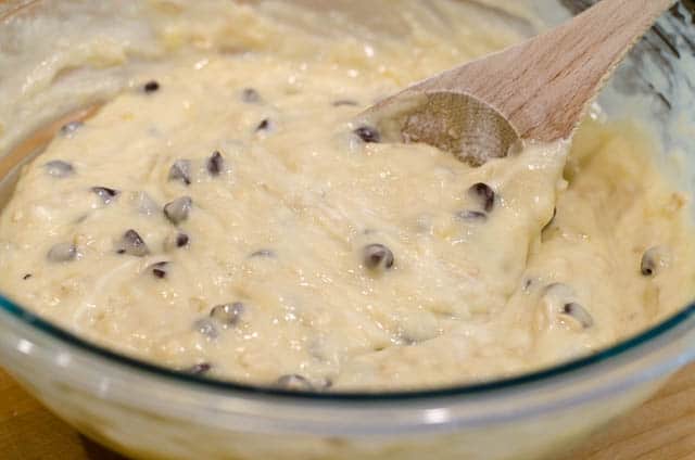 A wooden spoon stirs chocolate chips into the Banana Oatmeal Chocolate Chip Muffin batter.