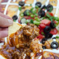 A close up of a tortilla chip scooping up beef enchilada dip.