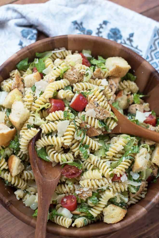 Chicken Caesar Pasta Salad in a wooden serving bowl with wooden serving spoons.