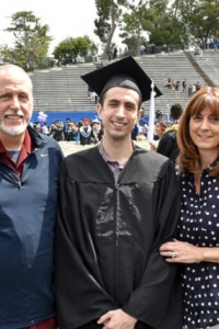 A young man wearing a graduation cap and gown with mom and dad on either side.