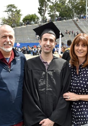 A young man wearing a graduation cap and gown with mom and dad on either side.