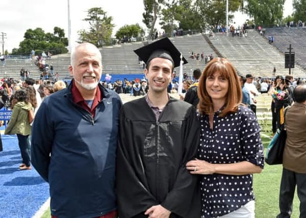 A young man wearing a graduation cap and gown with mom and dad on either side.