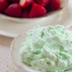 A bowl filled with green whipped cream with strawberries in the background.