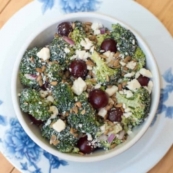 A bowl filled with broccoli, grapes and feta.