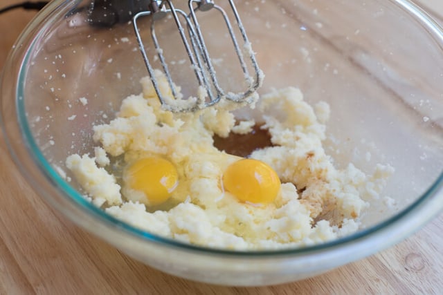 Eggs, sugar, butter, vanilla and almond extracts in a glass mixing bowl with the beaters from a hand mixer.