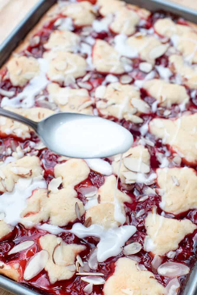 A powdered sugar glaze is drizzled over the bars with a spoon.