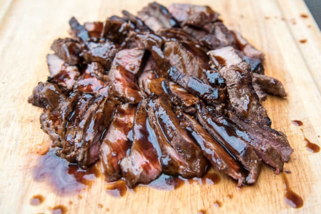 Sliced steak with teriyaki sauce on a cutting board.