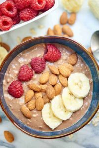 A bowl filled with overnight oats topped with raspberries, almonds, and bananas.