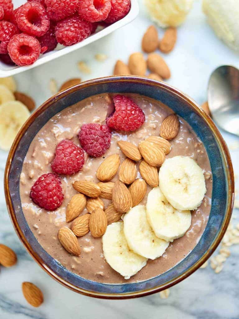 A bowl filled with overnight oats topped with raspberries, almonds, and bananas.