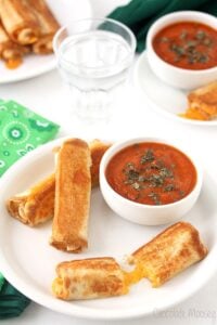 Grilled Cheese Rollups on a white plate with a small bowl of tomato soup.