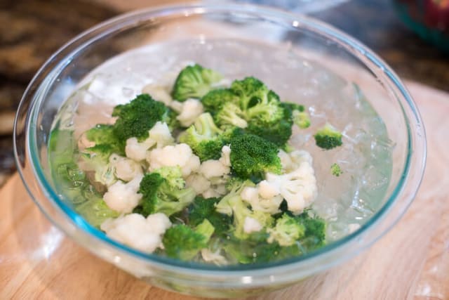 The partially cooked broccoli and cauliflower in a glass bowl of ice water.