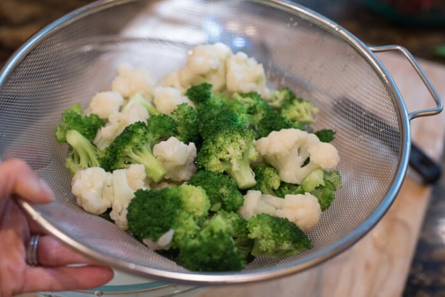 The broccoli and cauliflower in a mesh colander.