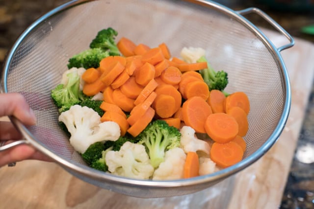 Partially cooked slices of carrot are added to the colander to drain.