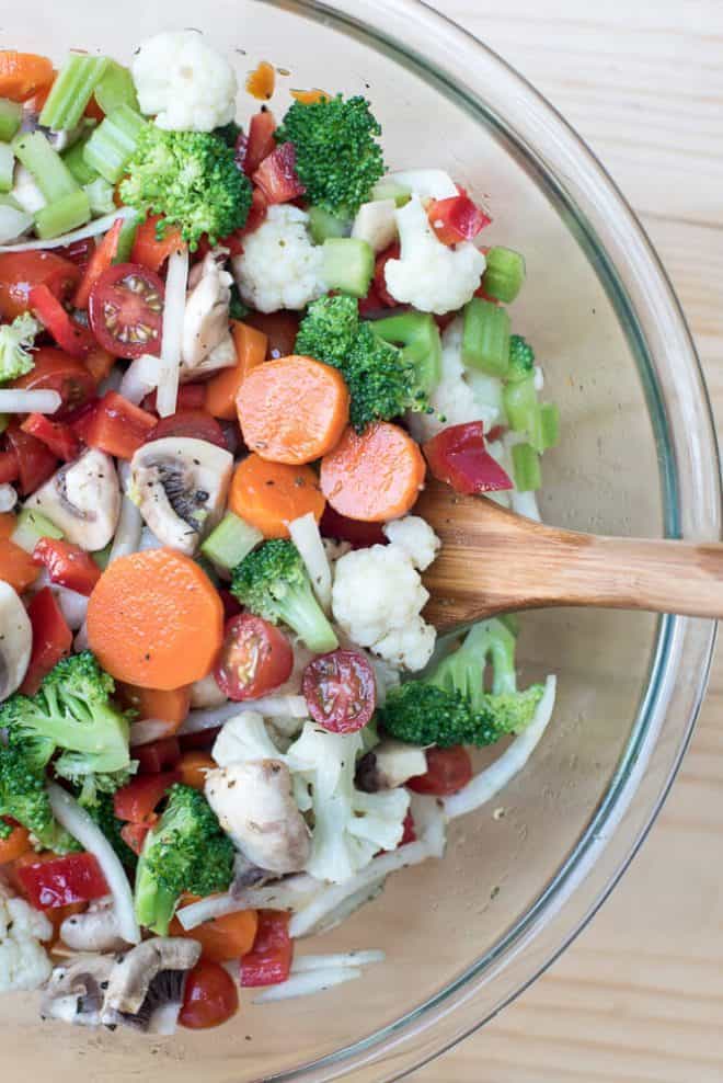 Marinated Vegetable Salad in a glass bowl with a wooden spoon.