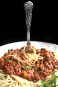 A fork twirling spaghetti with bolognese sauce on a white plate.