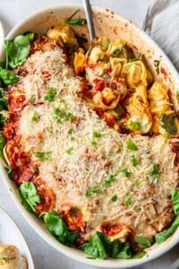 A spoon rests in a casserole of tortellini with spinach and Parmesan.