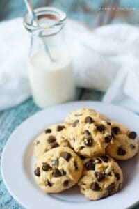A stack of chocolate chip cookies on a white plate in front of a glass of milk.
