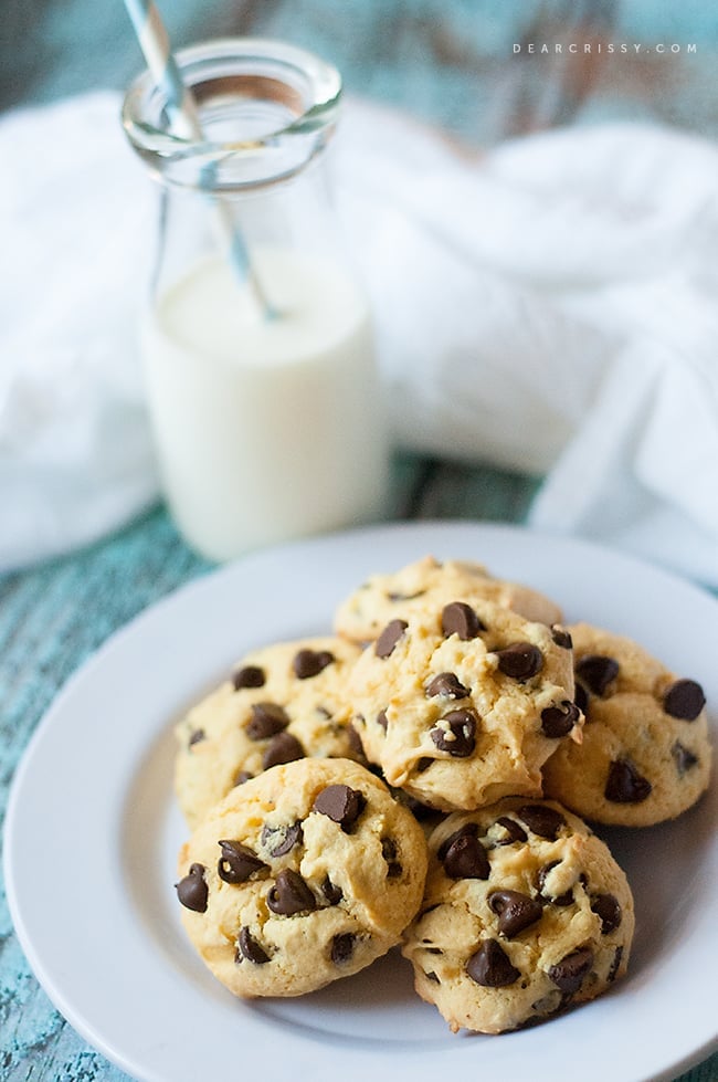 A stack of chocolate chip cookies on a white plate in front of a glass of milk.