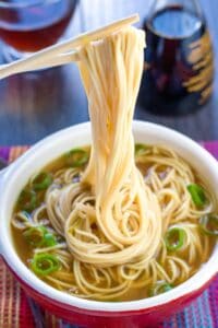 Chopsticks lift noodles from a bowl of soup.