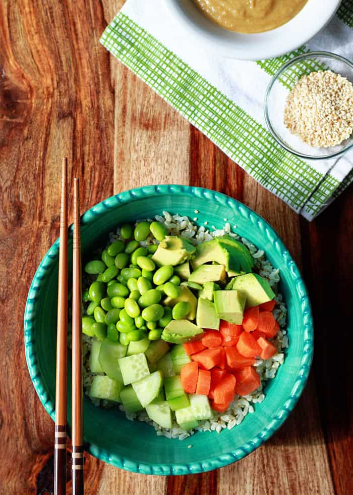 Chopsticks laying over the top of a sushi rice bowl with vegetables.