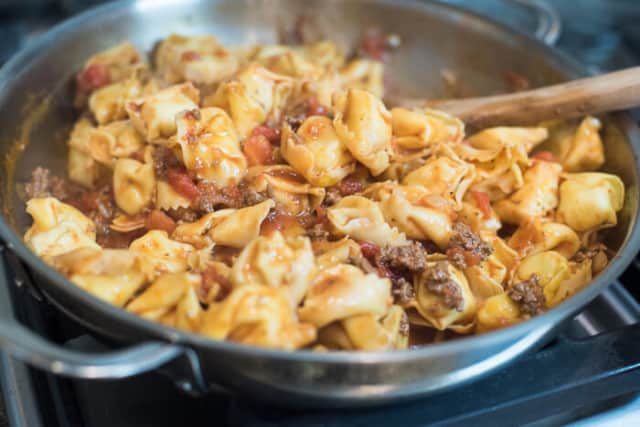 A wooden spoon stirs the mixture in the skillet.