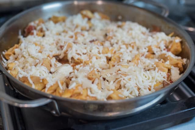 Cheese is sprinkled over the top of the mixture in the skillet.