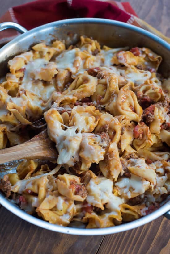 A wooden spoon scoops up some of the tortellini.