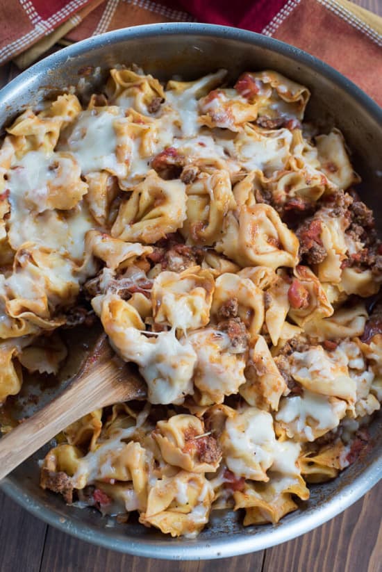 Cheesy Skillet Tortellini with Meat Sauce in a stainless steel skillet with a wooden spoon.