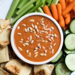 A bowl filled with roasted red pepper and white bean dip surrounded by veggies.