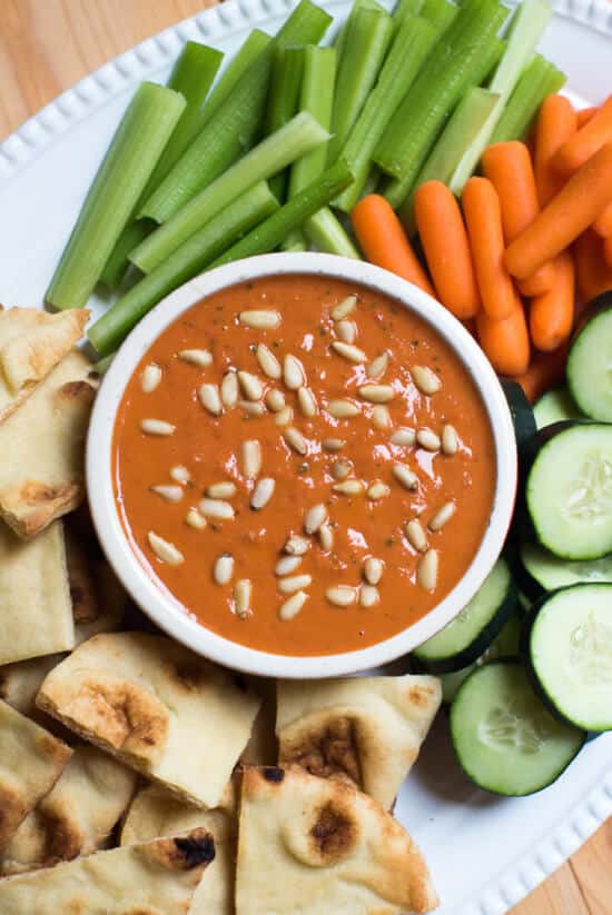 A bowl filled with roasted red pepper and white bean dip surrounded by veggies.