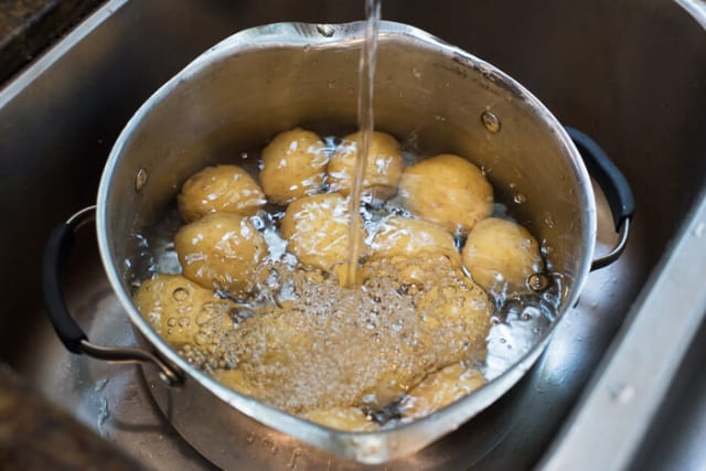 A pot filled with baby yellow potatoes in a sink being filled with water.