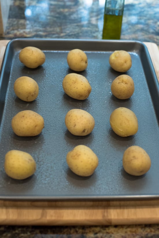 Yellow potatoes lined up on a greased baking sheet.