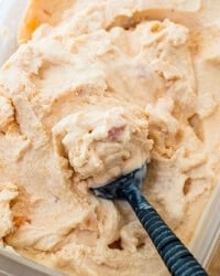 An ice cream scoop scoops up peach frozen yogurt.
