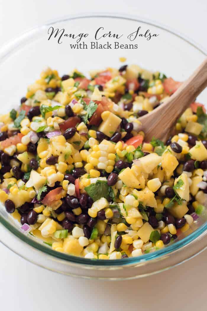 Mango Corn Salsa with Black Beans in a glass bowl with a wooden spoon with text overlay.