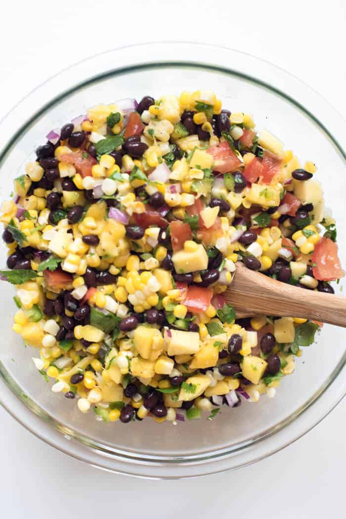 An over the top shot of Mango Corn Salsa with Black Beans in a glass mixing bowl with a wooden spoon.