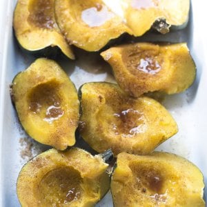 Pieces of cooked acorn squash topped with butter, brown sugar and cinnamon in a baking dish.