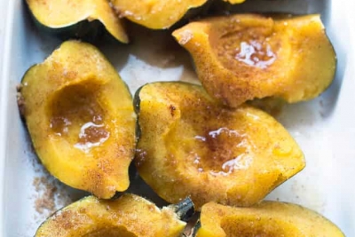 Pieces of cooked acorn squash topped with butter, brown sugar and cinnamon in a baking dish.