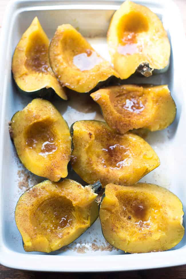 Pieces of cooked acorn squash topped with butter, brown sugar and cinnamon in a baking dish.