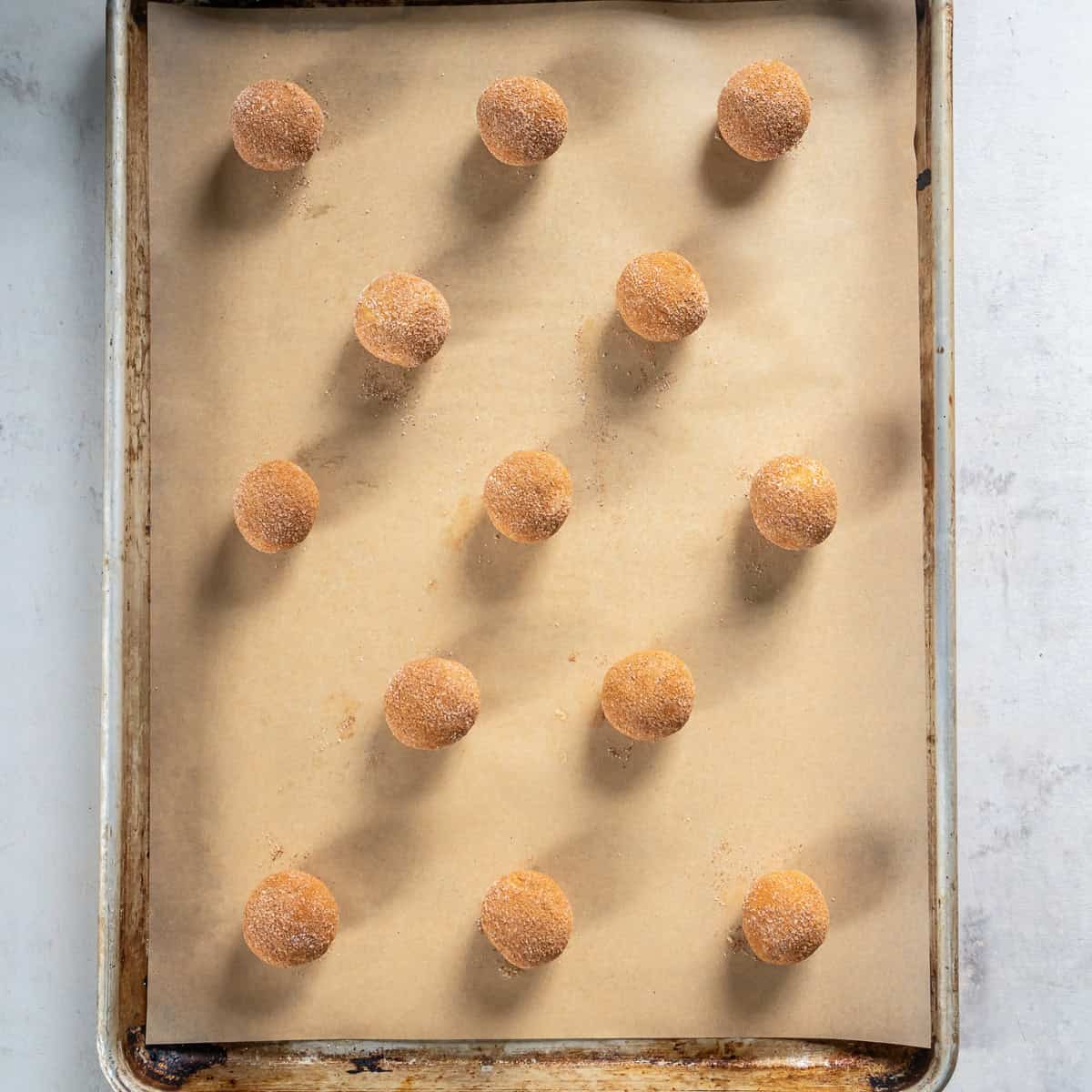 Spiced sugar-coated snickerdoodle dough balls spaced apart on a parchment-lined baking sheet.