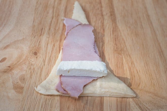 Sliced deli ham and a piece of mozzarella cheese placed on top of a piece of crescent roll dough.