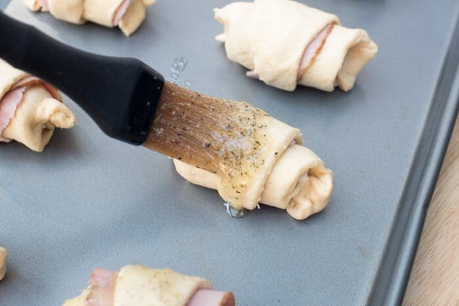 The butter mixture is brushed on to the stuffed crescent rolls.